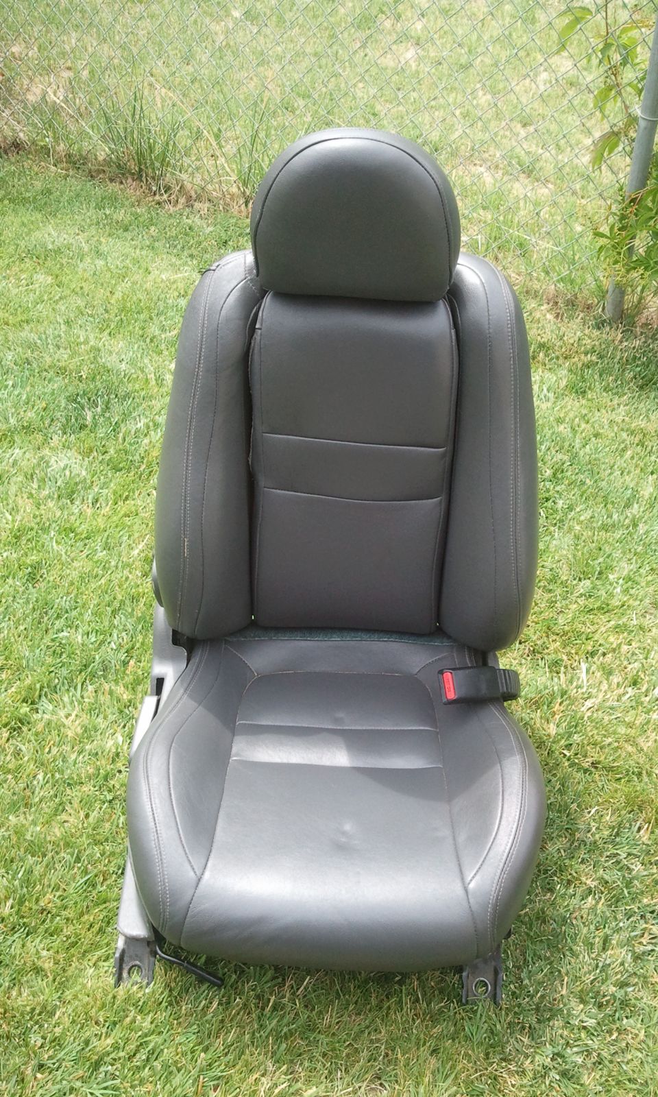 Black leather car seat with red seatbelt buckle, viewed from the front outdoors