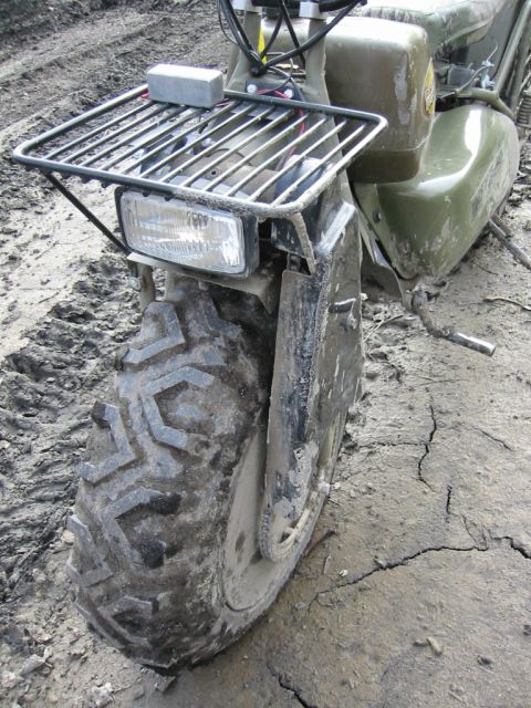 1985 Ford Bronco - An all-terrain vehicle sits in mud, its front tire and fender prominently displayed.