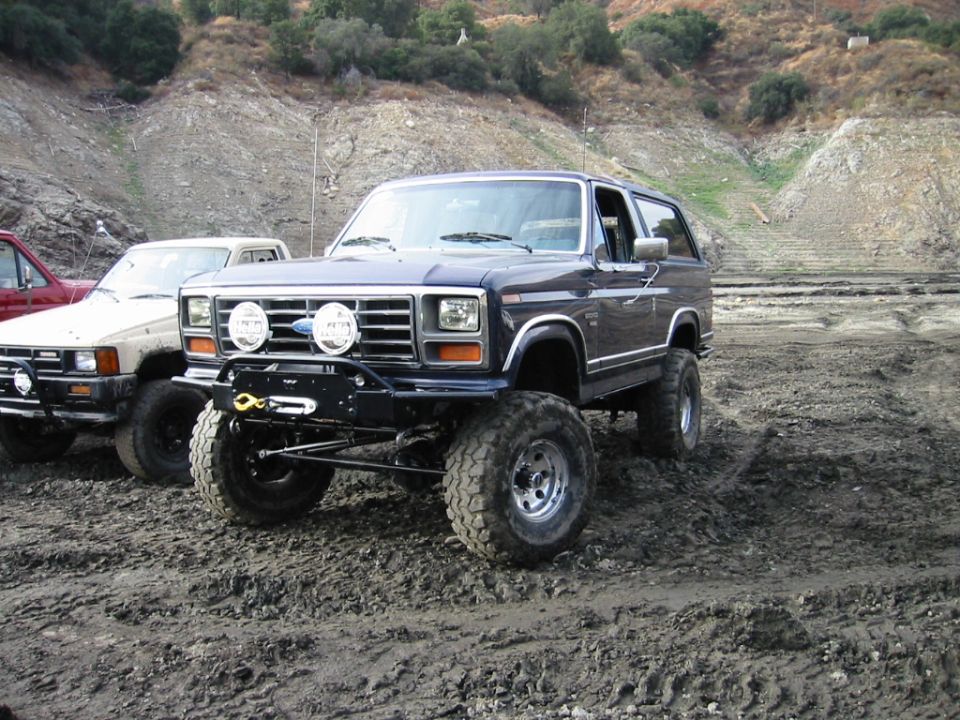 Dark lifted Ford Bronco SUV on mud tires parked in a muddy off-road area