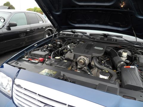 2003 Ford Crown Victoria - Engine compartment of a blue Crown Victoria, with a black sedan reflected at left under raised hood.