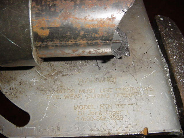 Metal part with "WARNING! OPERATOR MUST USE PROTECTIVE EYE WEAR DURING OPERATION" and "MODEL RYN 100 OIL JOINT JIGGER" text