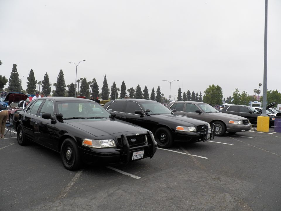 Black Ford Crown Victoria sedans parked diagonally with push bar at car show