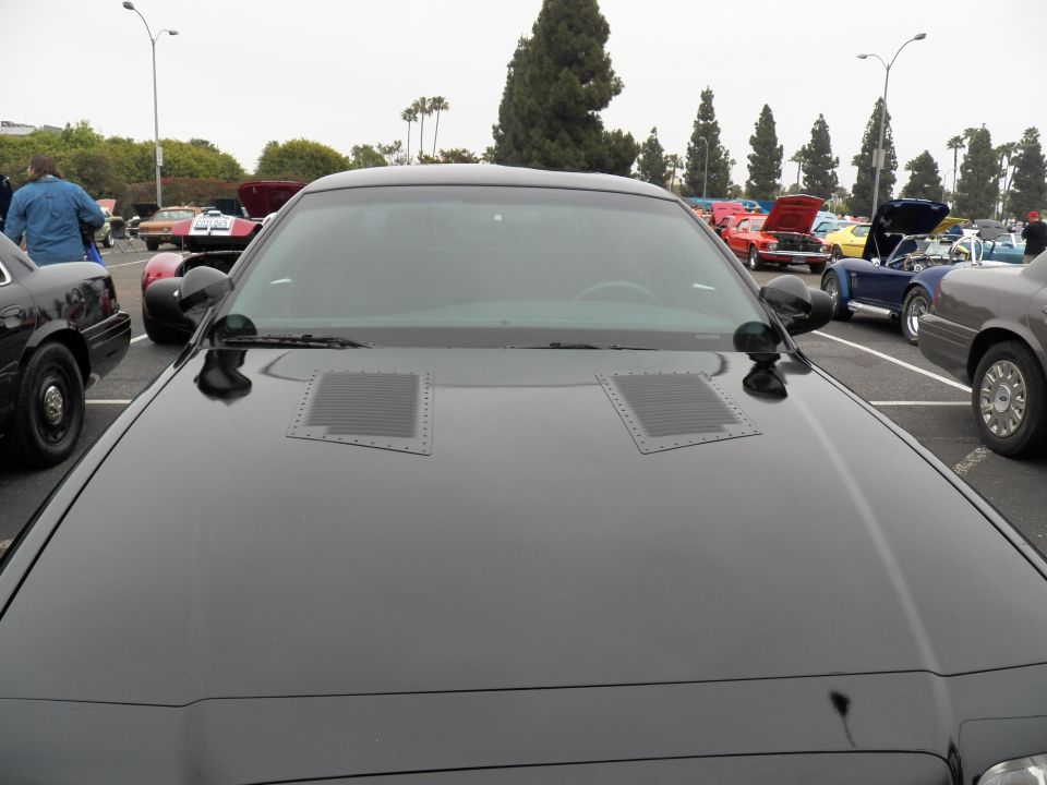 Black car hood with twin vents and windshield, vehicles behind at outdoor show