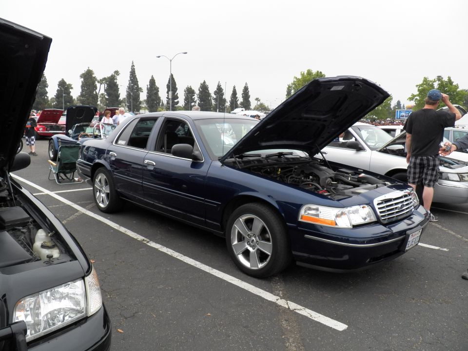 Dark blue Ford Crown Victoria sedan with hood open on alloy wheels at car show