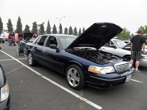 2003 Ford Crown Victoria - Front three-quarter of a navy Crown Victoria, hood open over engine, on polished alloys.