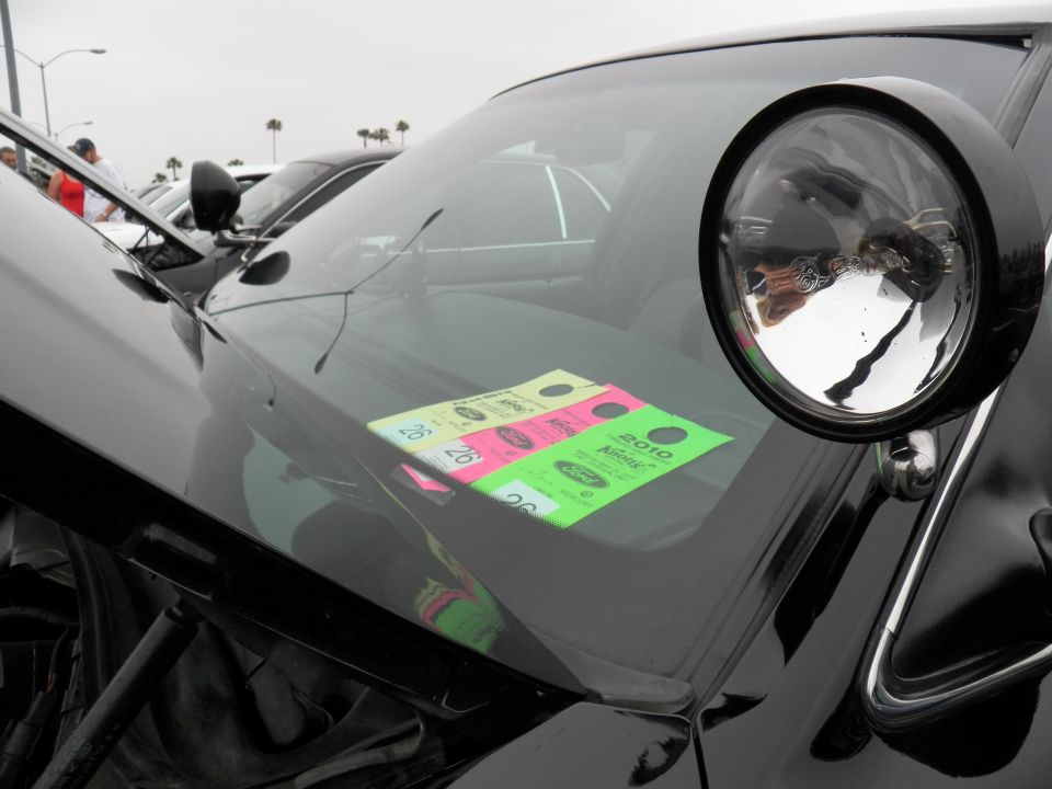 Round headlight and black fender of car with dealer event window stickers at outdoor car show