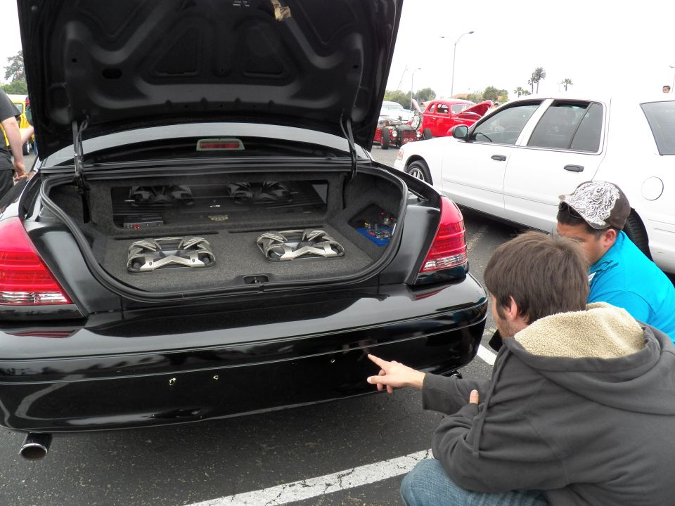 Open trunk of black Ford Crown Victoria showing dual subwoofers and amplifier audio install