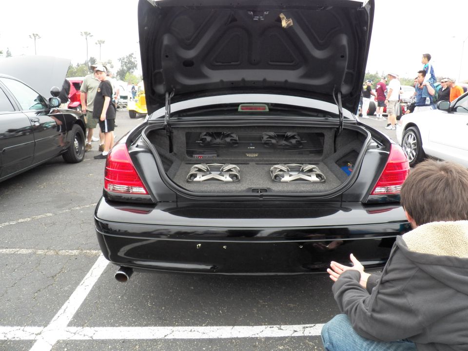 Rear view of black sedan with open trunk and dual subwoofer audio system at car meet