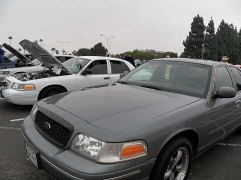 2003 Ford Crown Victoria - Front corner of a gray Ford sedan with blacked-out grille next to a white sedan with its hood open.