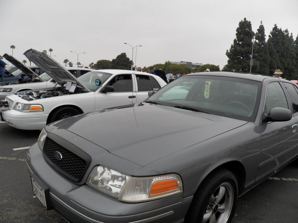 Gray Ford Crown Victoria front quarter view beside white sedan at outdoor car show