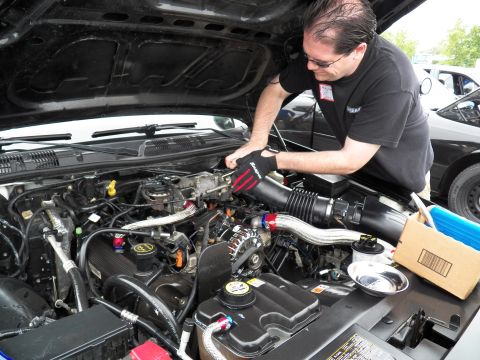 2003 Ford Crown Victoria - technician leans over an open engine compartment, polished intake piping and a parts box beside him.