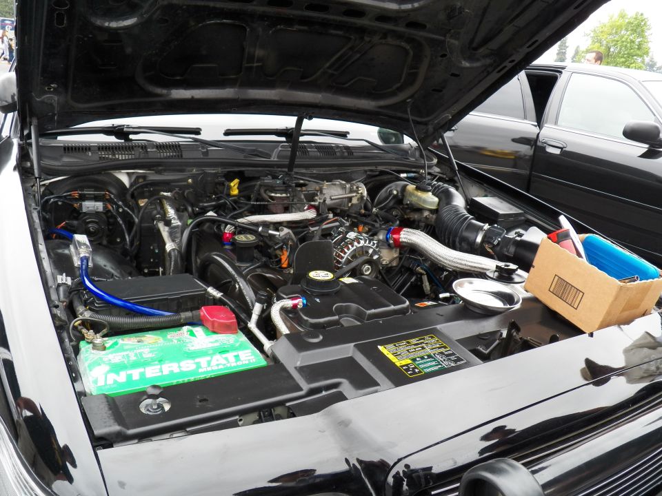 Engine bay with polished intake piping and Interstate battery in vehicle under raised hood