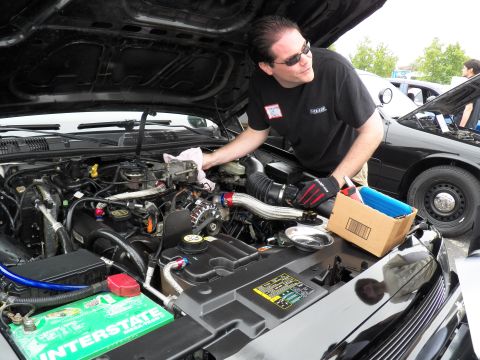 2003 Ford Crown Victoria - Technician in sunglasses cleans an engine fitted with polished intake tubing and a green Interstate battery.