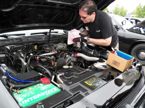 2003 Ford Crown Victoria - Man wipes down an engine compartment with polished intake piping, parts box and Interstate battery present.