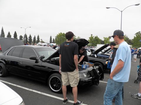 2003 Ford Crown Victoria - lowered black sedan on black wheels sits with its hood up beside other vehicles at an outdoor show.