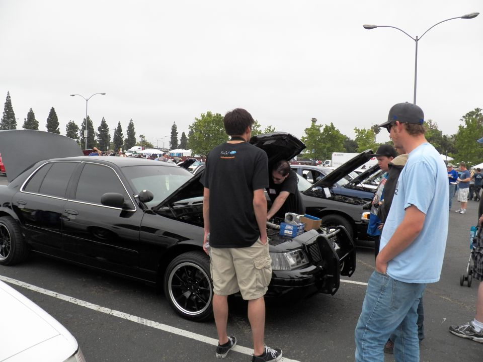 Black sedan with open hood beside other cars in a parking-lot car show