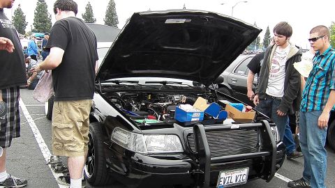 2003 Ford Crown Victoria - Onlookers study the engine of a black sedan with front push bar and EVIL VIC plate at a meet.