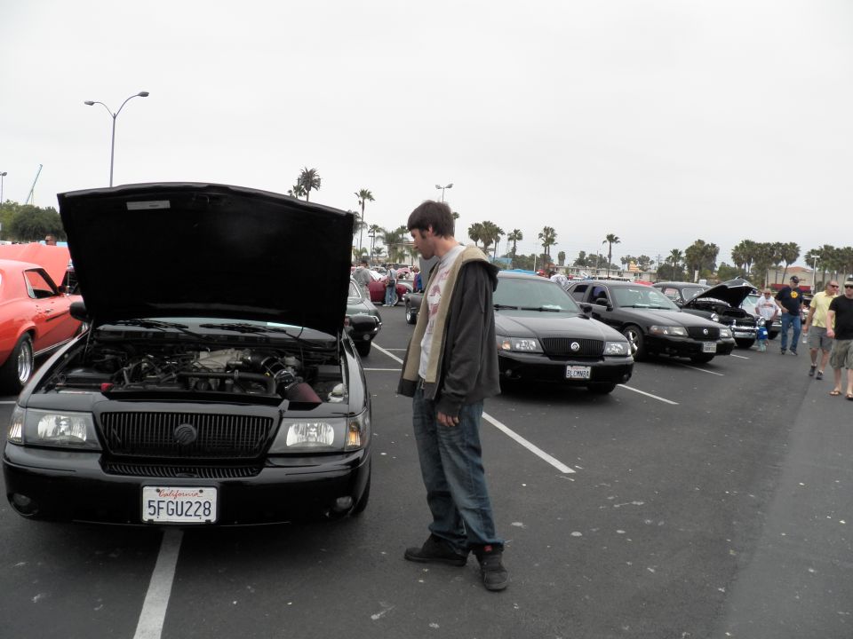 Black Mercury Grand Marquis with hood up at outdoor car show, man inspecting engine