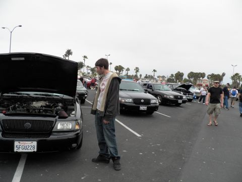 2003 Ford Crown Victoria - young man stands beside a black Mercury sedan with its hood open among rows of parked show vehicles