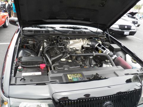 2003 Ford Crown Victoria - Open engine compartment of a black sedan showing a V8 with aftermarket conical air filter at a show