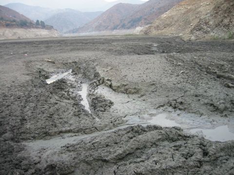 1985 Ford Bronco - The image depicts a desolate, muddy landscape with visible tire tracks, suggesting off-road vehicle activity in a dry riverbed or lakebed.
