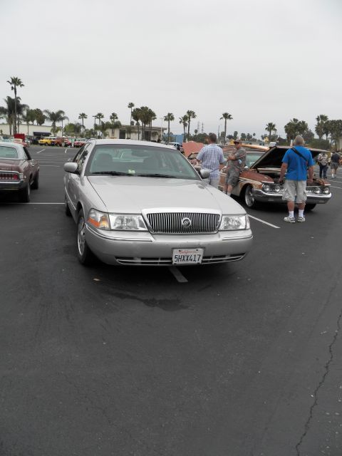 2003 Ford Crown Victoria - silver Mercury Grand Marquis sedan parked head-on among show cars with palm trees behind
