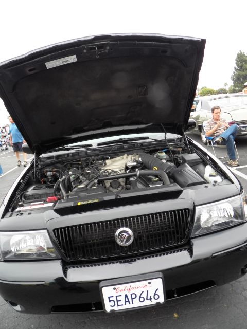 2003 Ford Crown Victoria - Front three-quarter view of a black Mercury with raised hood exposing its V8 engine at an outdoor meet