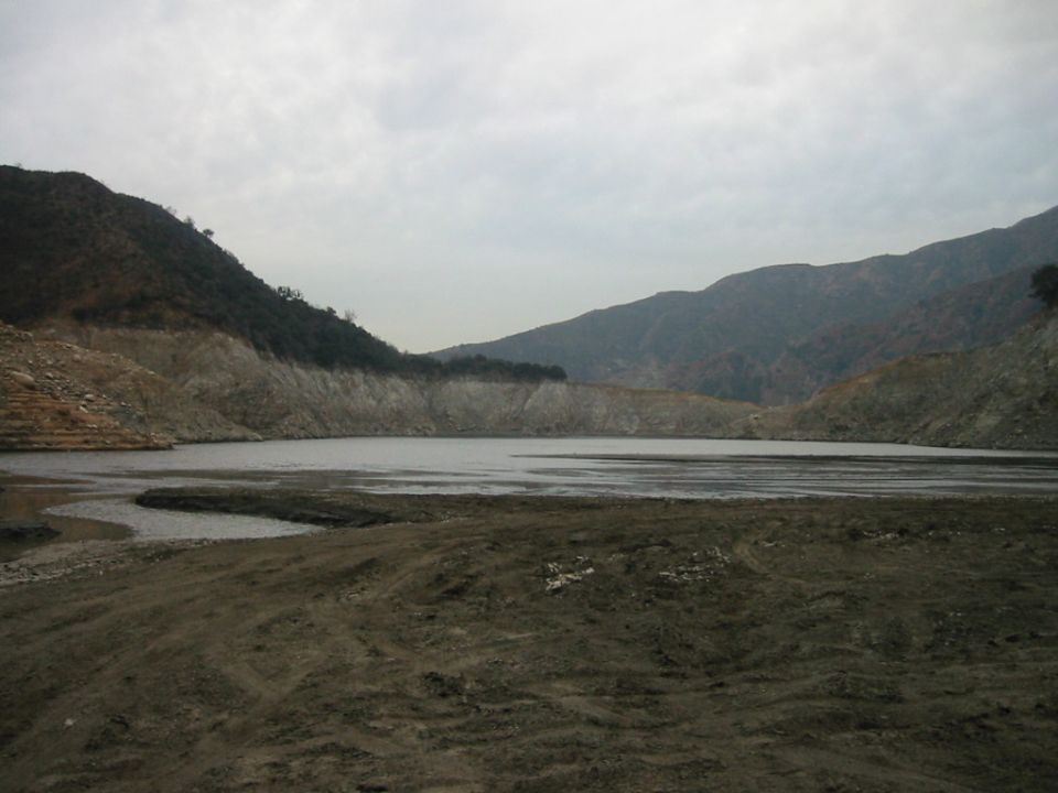 Low reservoir with muddy shoreline and hills under overcast sky