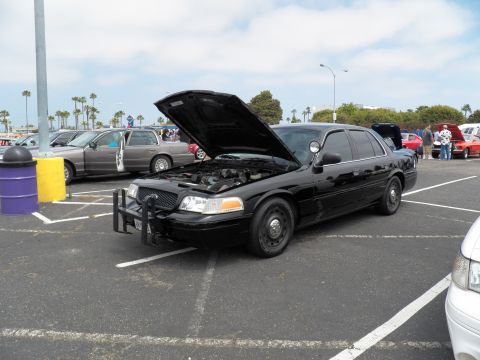 2003 Ford Crown Victoria - Hood-open black Crown Vic Police Interceptor parked in a lot beside other show cars and a tan sedan