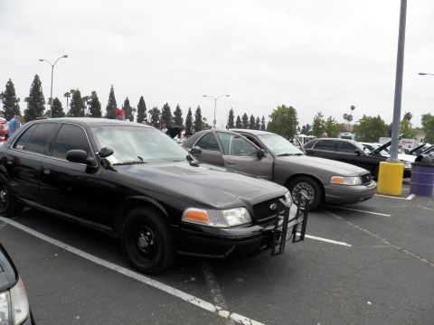 2003 Ford Crown Victoria - Black Crown Vic with steel wheels and push bar parked next to a gray Crown Victoria at a show