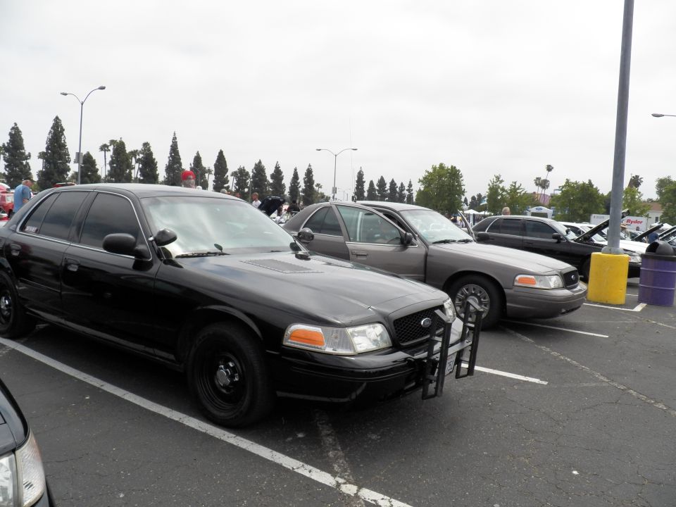 Black Ford Crown Victoria with push bar beside gray sedan in parking lot