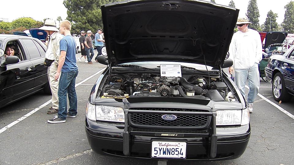 Black Ford Crown Victoria with open hood and push bar marked Code 3 at car show