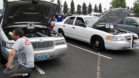 2003 Ford Crown Victoria - Man kneels by silver Mercury with Nevada DEWGONG plate; white Crown Vic alongside, both hoods up