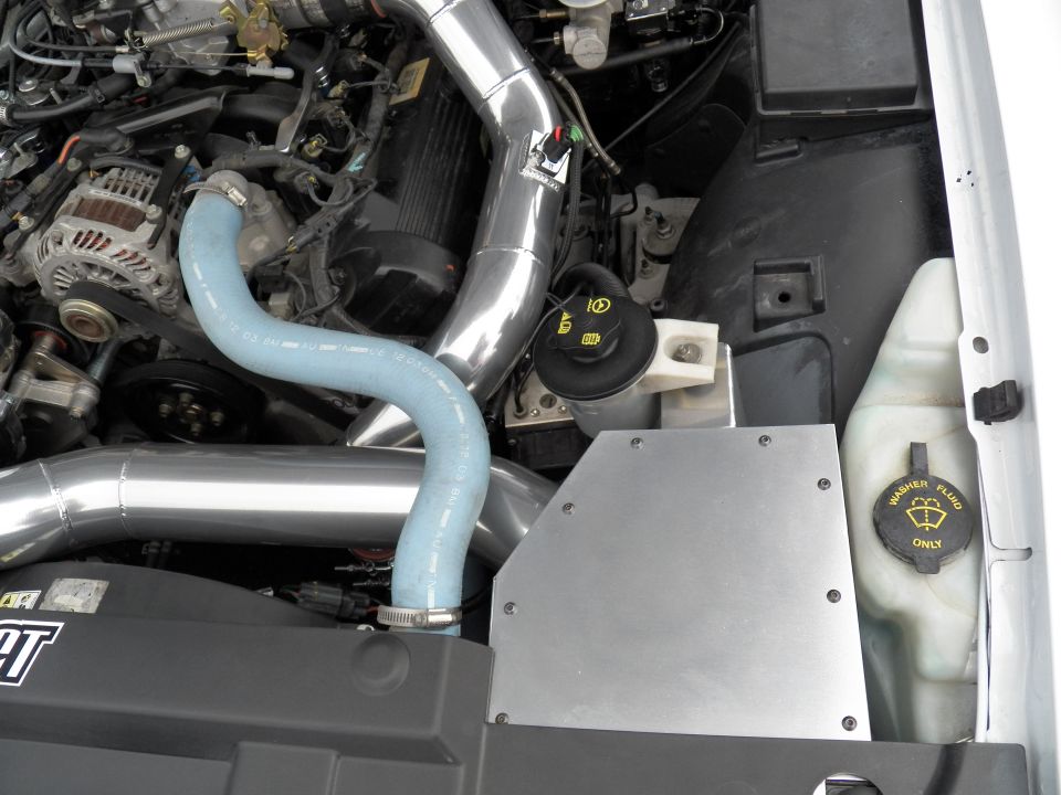 Engine bay corner with chrome intake tube, blue hose and washer fluid reservoir