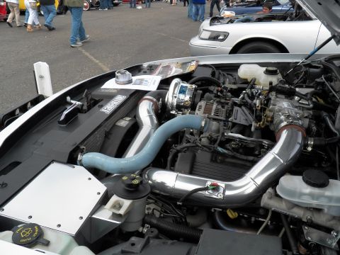 2003 Ford Crown Victoria - Open hood revealing twin polished intake tubes and supercharger; white sedan visible behind