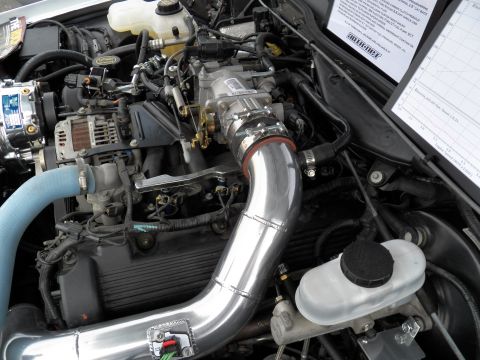 2003 Ford Crown Victoria - Forced-induction modified V8 under the hood, polished cold-air piping routed to a supercharger, spec card propped at right.