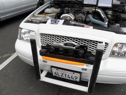 2003 Ford Crown Victoria - Front grille of a white Ford sedan reads BLUE, hood up over a blower build; CA plate 6LZT449 and a Vortech display board visible.