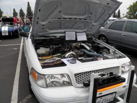 2003 Ford Crown Victoria - White Ford sedan hood raised over a turbo or blower swap, The Rocket Couch decal on fender, spec sheets propped on the engine.