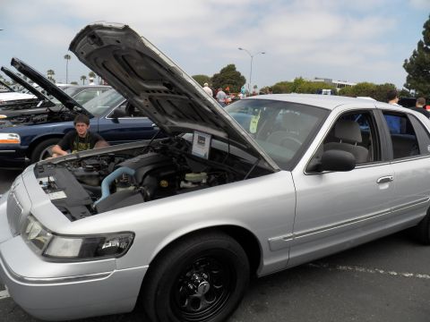 2003 Ford Crown Victoria - Silver Panther-platform sedan parked with hood raised, black steel wheels, a spectator leaning into the engine bay.