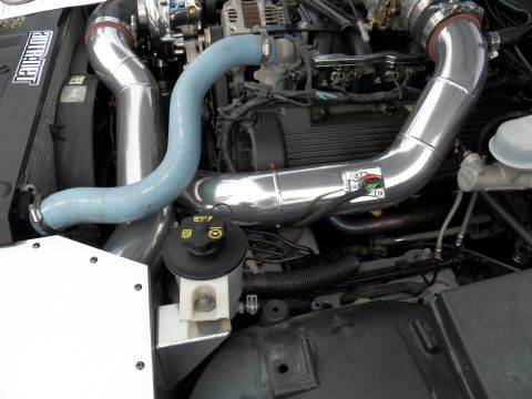 2003 Ford Crown Victoria - Twin polished intake pipes and a blower over a Ford V8, blue coolant hose at left, white power-steering reservoir below.