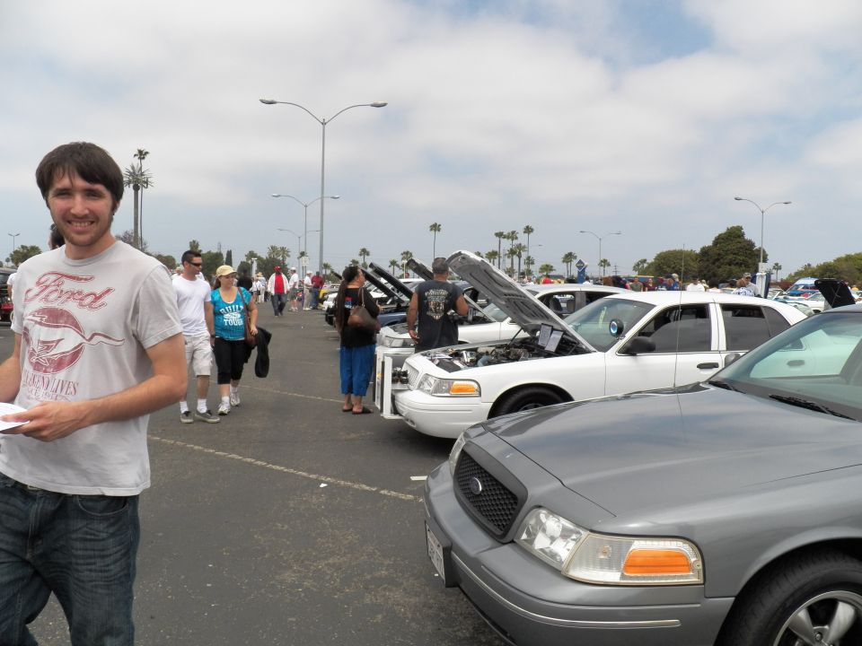 Man in Ford shirt at car show with white Crown Victoria sedans behind