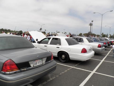 2003 Ford Crown Victoria - Gray Crown Victoria with CHP P71 plate foreground, white Panther sedans receding in the parked row under an overcast coastal sky.