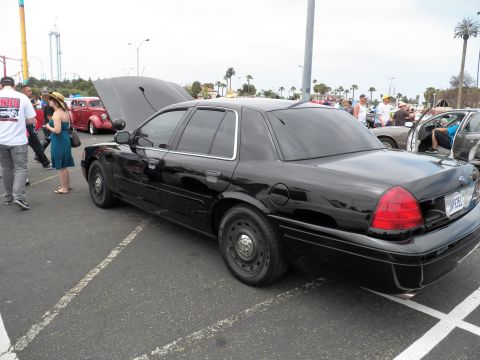 2003 Ford Crown Victoria - Black Crown Victoria displayed hood-up; woman in teal dress and crowd in lot behind