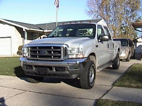 2004 Ford F-250 - A silver 2004 Ford F-250 pickup truck is parked in a driveway with a house and another vehicle in the background.