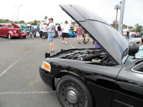 2003 Ford Crown Victoria - Black Crown Victoria displayed hood-up; spectators and red hot rod in the lot behind