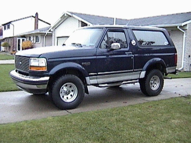 Dark blue two-door Ford Bronco with silver two-tone and chrome wheels parked on a driveway