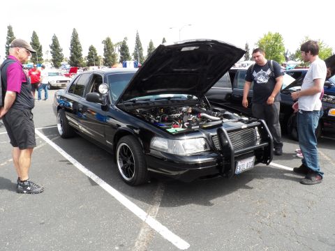 2003 Ford Crown Victoria - Side view of a black Ford sedan displayed open-hood as two men look on