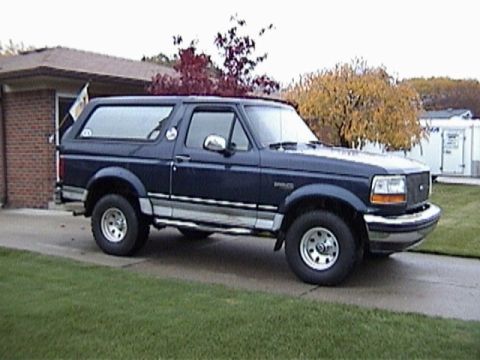 1995 Ford Bronco - This Ford Bronco is parked on a driveway next to a lawn and a brick building.