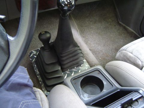 1989 Ford Ranger - The interior of a vehicle shows a center console with dual gear shifters and a cup holder.