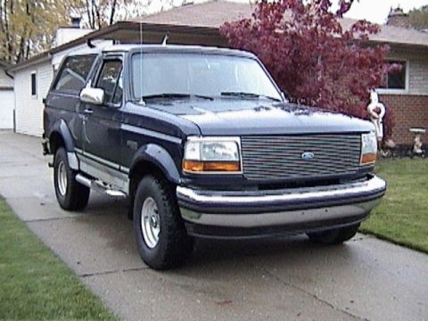 1995 Ford Bronco - Front three-quarter view of a dark blue two-door Ford Bronco with a silver lower two-tone, chrome grille with blue Ford oval, chrome bumper…